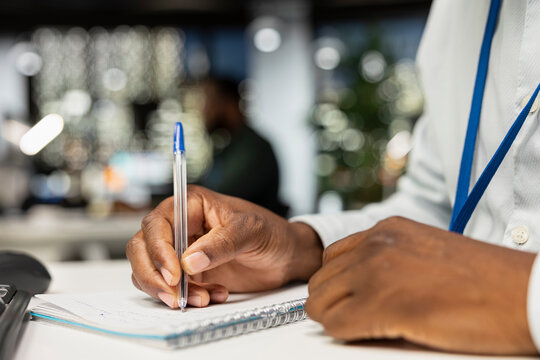 Close up of black businessman transcribing key points on notebook after hours. Employee creating a summary, proofreading numbers and designing strategy to align with company targets.