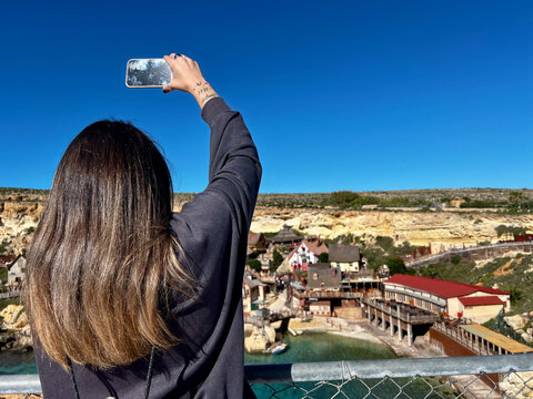 Tourist taking photo of popeye village in malta with smartphone