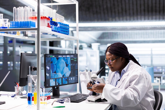 African american chemist analyzing molecular samples in a lab, using professional microscope. Healthcare innovation and biochemistry experiments represent scientific method and discovery.