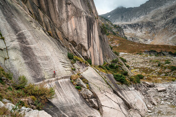 A lone hiker walks along an exposed trail carved into a steep cliff in the Swiss Alps, ideal for adventure travel themes © PietFoto
