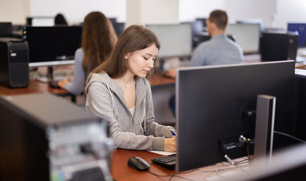 Young woman taking notes while working on computer in office space