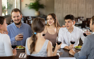 Obraz premium Group of men and women friends eating drinking and talking in restaurant