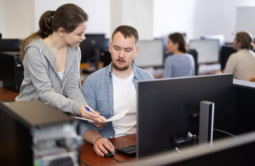 Obraz premium Young man and young women discussing document while working on computer in office space