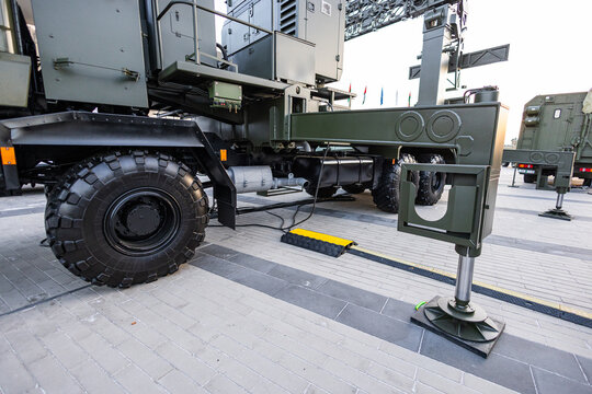 Military equipment and army equipment.. Wide shot military command platform deployed with outriggers extended on urban pavement, support legs anchored, vehicle fleet in background,