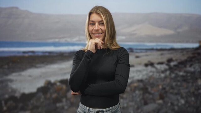 Woman, young blonde, smiling with hand on chin and arms crossed, posing in studio with beach backdrop; confidence contemplation.
