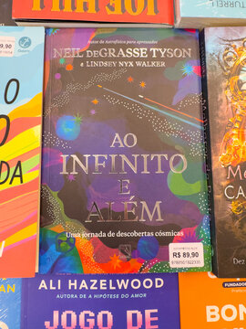 The captivating dark blue cover of Ao Infinito e Al&eacute;m by Neil deGrasse Tyson and Lindsey Nyx Walker, featuring cosmic imagery, is displayed in a bookstore