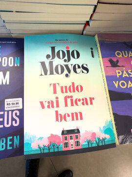 BELO HORIZONTE, MG, BRAZIL, MARCH 31, 2026. The cheerfully optimistic pastel-colored cover of Jojo Moyes's novel "Tudo vai ficar bem," featuring a small house and trees, is displayed in a bookstore.