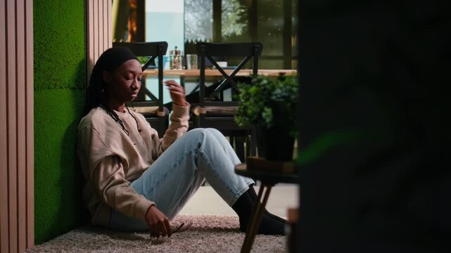 Unhappy black woman in depressive mood suffering from stress and frustration, sitting silently on the floor in hallway, mental illness and emotional breakdown. Sad girl in sorrow, darkness.