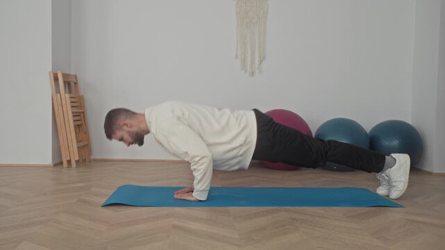 Man on blue mat performing pushup with hands under chest in studio; focus balance stability control.