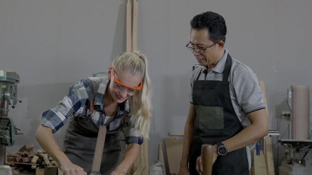 Woman man carpenter workshop woodworking safety glasses apprentice instructor training teamwork focused carpentry using hand tools chisel mallet apron protective eyewear furniture making wood carving