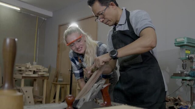 Carpenter woodworking workshop safety hand plane teamwork apprentice instructor craft tool training, male and female carpenters shape timber board with hand tool, wearing apron and safety glasses