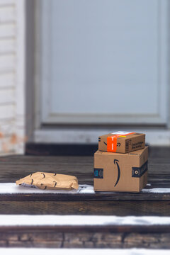 Calgary, Alberta, Canada. April 9, 2026. Vertical view of an Amazon Prime cardboard boxes and a mailer sit on a snowy wooden porch after home delivery.