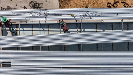 Naklejka premium Aerial view of construction workers installing roofing panels on a building, surrounded by tools and materials, showcasing teamwork, precision, and the construction process in progress.