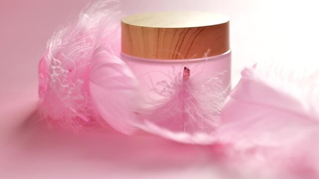 cosmetic jar with a wooden lid surrounded by soft pink feathers. product mockups, branding, natural cosmetics, and wellness concepts. 4k footage