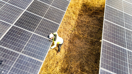 Focused construction worker installing photovoltaic solar cell modules on the ground. Eco friendly...