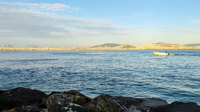 Panoramic View of Istanbul Skyline and Marmara Sea from Kinaliada Shore with a Small Fishing Boat, Flying Seagull, and Rocky Coastline Under a Blue Sky during Golden Hour - Turkey