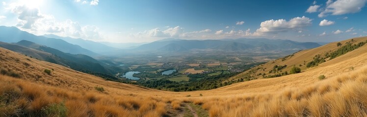 Fototapeta premium Wide Balkan mountain valley panorama with dry golden grass slopes, lakes and rural village. Clear summer sky over hazy mountain range in distance. Blue sky with soft white clouds above.