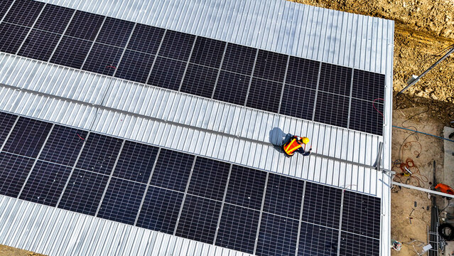 A worker wearing safety gear installing solar panels on a rooftop with nearby housing units in the background, emphasizing renewable energy, sustainability, and efficient solar power implementation