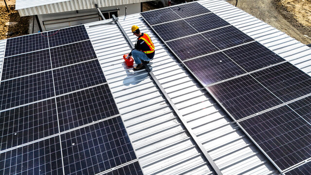 A worker wearing safety gear installing solar panels on a rooftop with nearby housing units in the background, emphasizing renewable energy, sustainability, and efficient solar power implementation