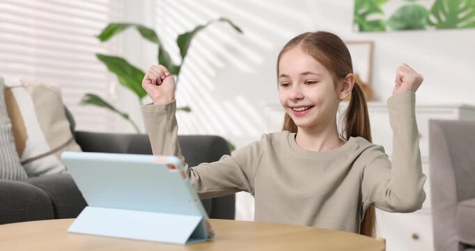 Little girl using tablet at wooden table at home