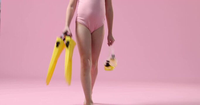 Little girl in swimsuit with fins and mask on pink background, camera moving down