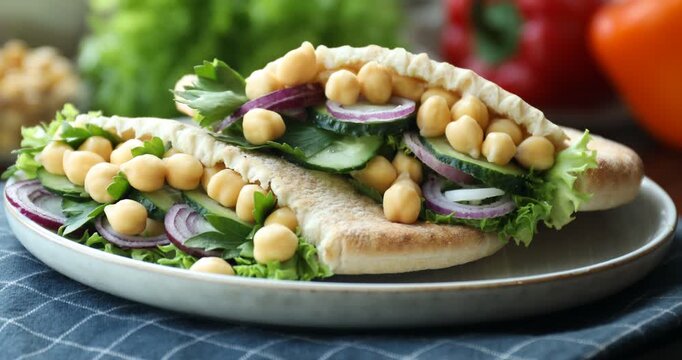 Plate with pieces of tasty pita bread with chickpeas, parsley and vegetables turning against blurred background, closeup