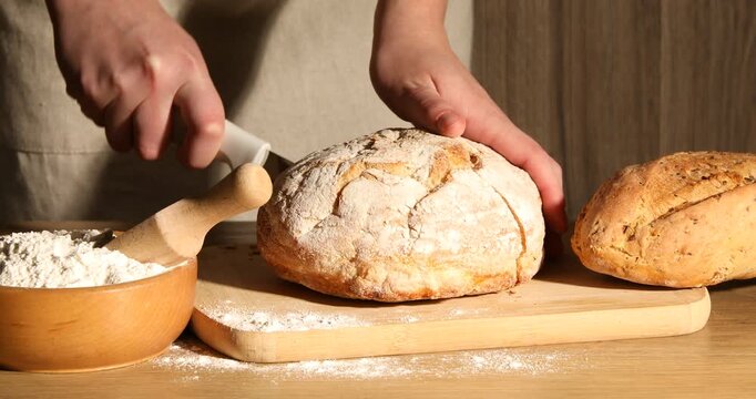 Woman cutting fresh bread at wooden table, closeup