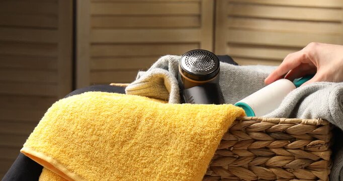 Woman putting fabric shaver and lint roller into basket with clothes indoors, closeup