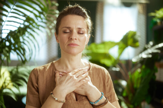 A woman centers herself with a mindful self-soothing gesture, focusing on her internal state to find emotional balance and peace within her indoor sanctuary.
