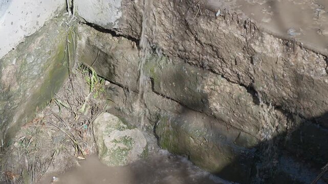 Dilapidated water drainage. Cracked wall with algae growth. Moss and grime signal drainage issues. Environmental neglect causes decay and environmental deterioration visible