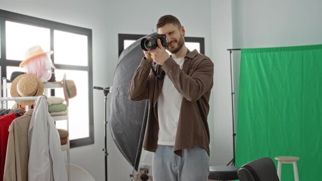 Man photographer adjusts camera settings and raises camera to eye amid green screen and softbox lighting in studio; concentration creativity.