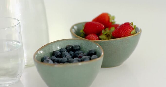 Camera moving forward sharpening focus bringing teal bowls with blue red berries closer on tabletop