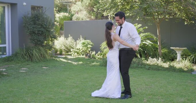 Newlyweds celebrating wedding in yard groom reaching, spinning bride in white gown friends hugging