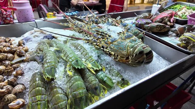 A vibrant close up shot of various fresh seafood including large lobsters mantis shrimp and tied crabs displayed on ice at a street food market stall in Bangkok Thailand during the evening
