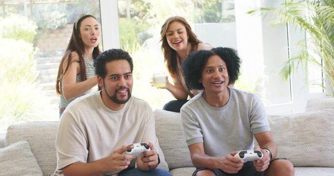 Diverse friends reacting to surprise while two men playing game on couch holding white controllers