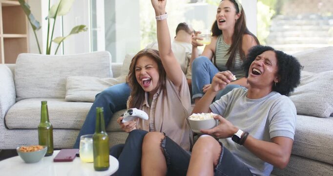 Diverse friends reacting to game event on couch by window, front woman celebrating with controller