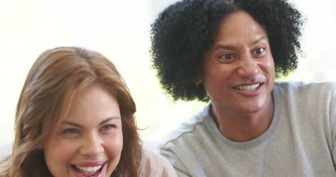 Couple sitting on sofa leaning in watching game, woman holding white controller after landing win