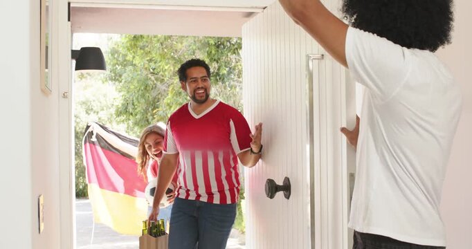 Vertical video: Diverse fans entering door man in red kit with drinks flag waving joining party hug