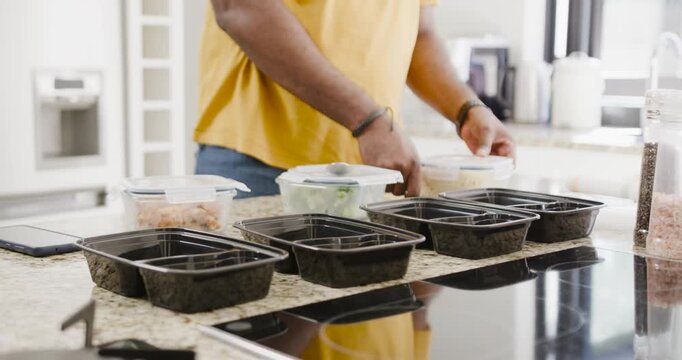 Man placing black trays at counter, scooping food from clear tubs, preparing meals