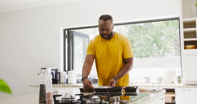African man leaning picking lids pouring jug sealing black trays prepping food on island near stove