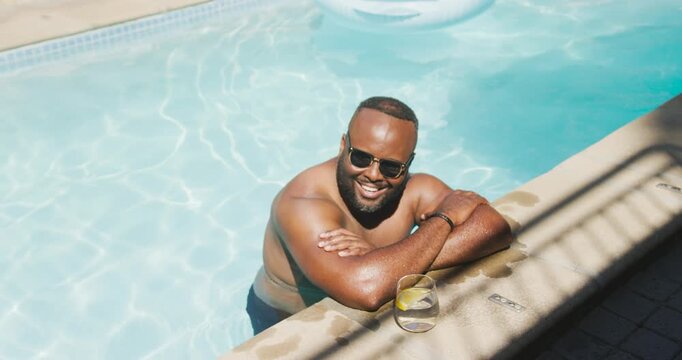 Mid-adult African American man smiling at camera, then reaching for stemless lemon glass to sip