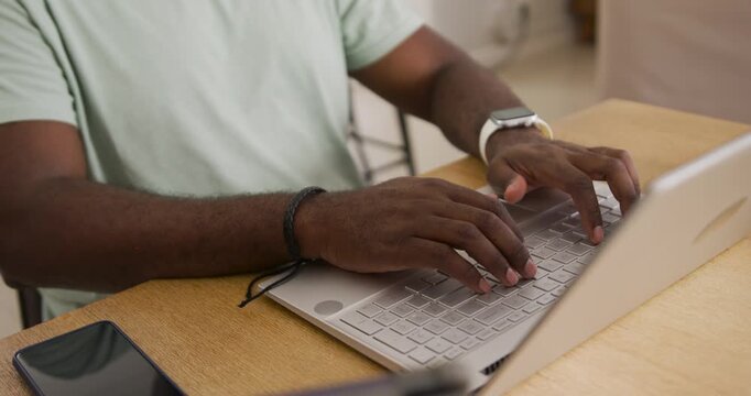 Mid adult African man placing hands on laptop keyboard, typing and working at wooden table