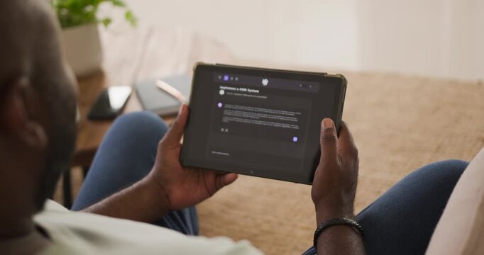 African American man sitting on couch holding tablet, adjusting grip to read dark settings screen