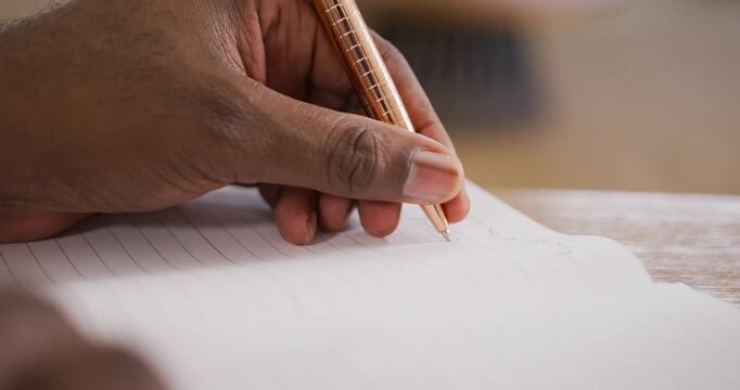 African American man pausing after jotting notebook-notes with pen typing to save on laptop at desk
