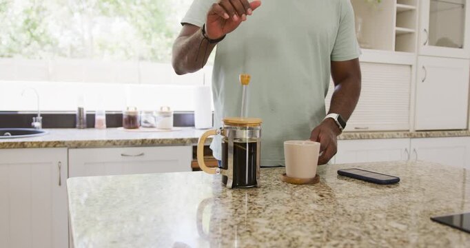 African American man pressing French press plunger on granite island brewing java smartphone nearby
