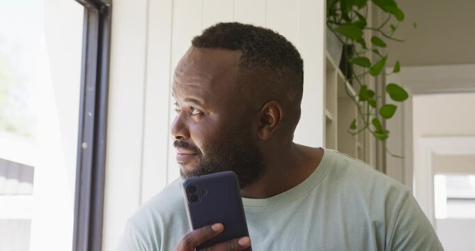 Midadult African man squinting raising phone reading message at home by bright window in green tee