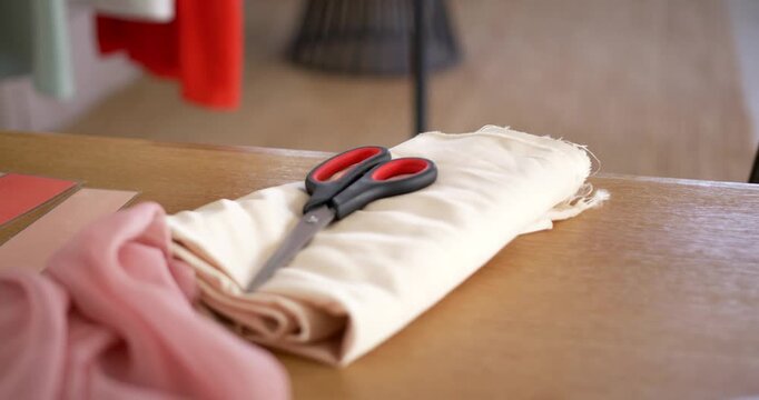 Folded beige fabric with scissors black handles red grips resting on tabletop, pink cloth at left