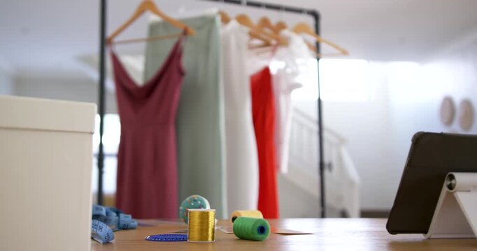 Camera tilting up, revealing four dresses and spools with tablet in sewing studio showing garments