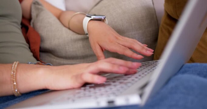 Two female friends collaborating, typing on laptop on couch, wearing white watch and gold bracelets