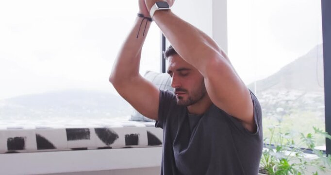 Adult man lowering joined palms from overhead to forehead near window for meditation, smartwatch